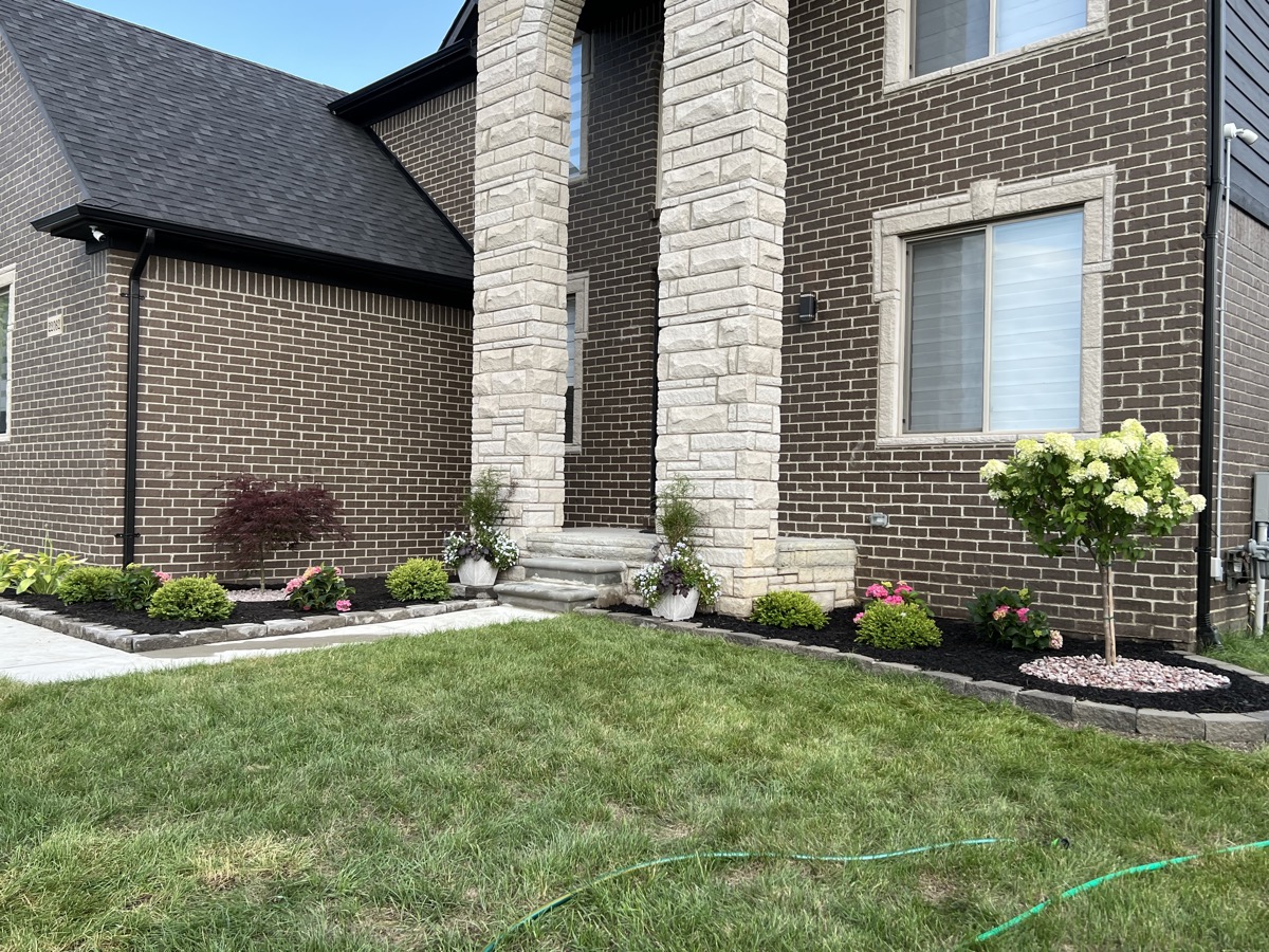 Front yard landscaping with garden beds, boxwood, retaining wall, and flower plantings